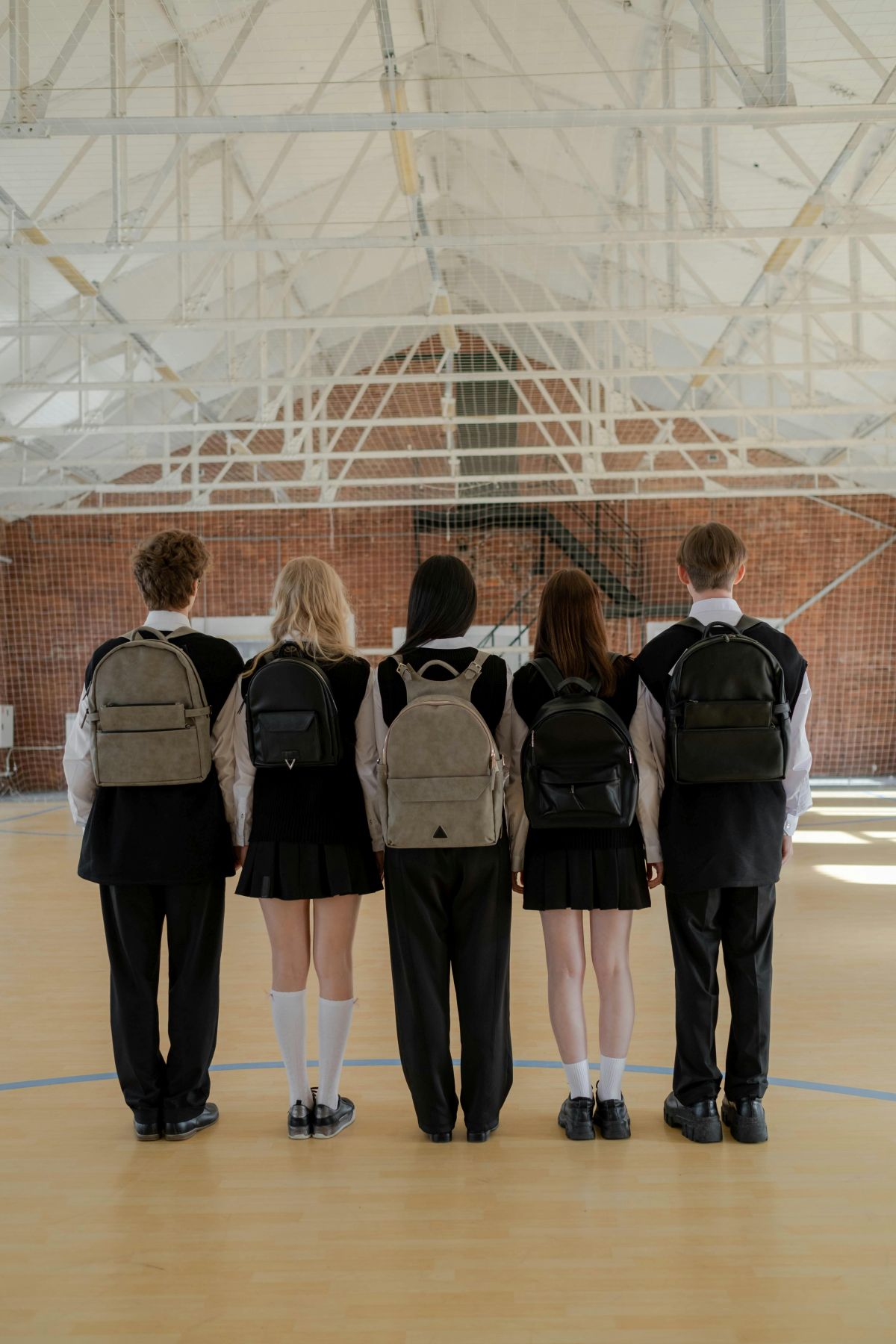 Fünf Schülerinnen und Schüler einer Secondary School in den USA stehen mit Schuluniformen und Rucksäcken in einer Turnhalle und blicken nach vorn.